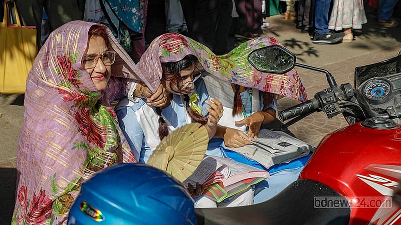 কেন্দ্রে প্রবেশের অপেক্ষায় থাকা সন্তানদের রোদ থেকে রেহাই দিতে আঁচলে ঢেকে নিয়েছেন এক মা। ছবি: মাহমুদ জামান অভি