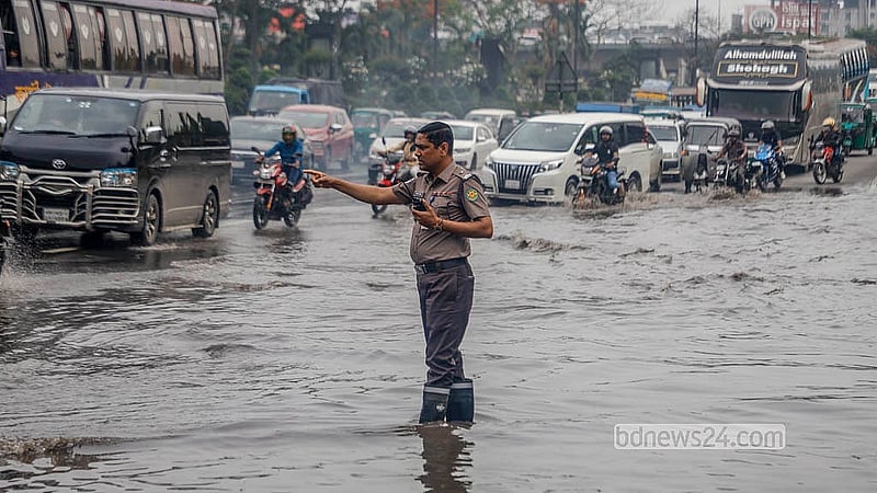 রাজধানীর বিমানবন্দর সড়কের নিকুঞ্জ এলাকায় জমে থাকা পানির মধ্যে দাঁড়িয়ে মঙ্গলবার দায়িত্ব পালন করেন ট্রাফিক পুলিশ সদস্যরা