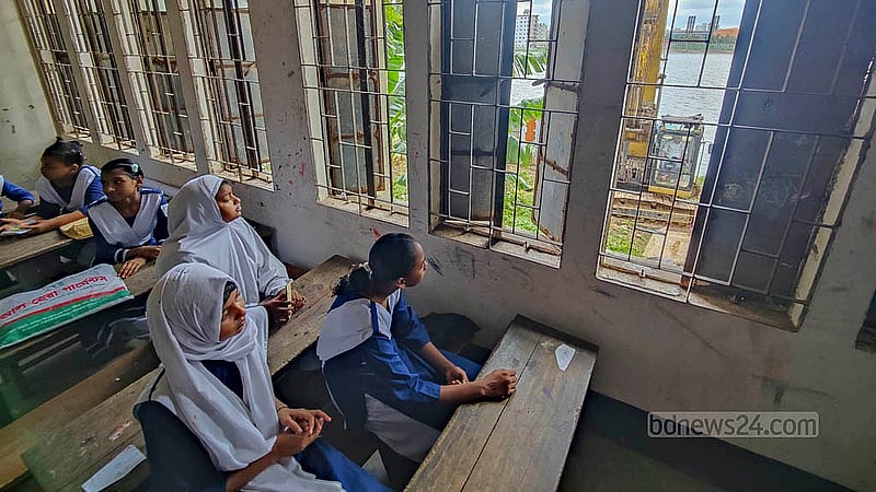 ঢাকার বছিলা সরকারি প্রাথমিক বিদ্যালয়ের পেছনে নদীর পাশ দিয়ে ওয়াকওয়ে বানাচ্ছে পানি উন্নয়ন বোর্ড। সেই কাজে ব্যবহার হচ্ছে স্কেভেটর, এ যন্ত্রের বিকট শব্দের মধ্যে ক্লাস করছে শিক্ষার্থীরা