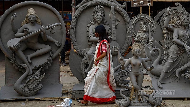 ঢাকার রমনা কালী মন্দিরে সারি করে রাখা সরস্বতী প্রতিমা ঘুরে দেখছেন এক নারী
