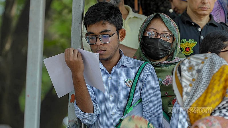 পরীক্ষা কেন্দ্রের বাইরে শেষবারের মত চোখ বোলাতে ব্যস্ত পরীক্ষার্থী, পাশেই দাঁড়িয়ে তার মা। ছবি: মাহমুদ জামান অভি