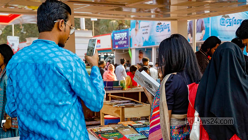 বই কেনার জন্য নয়, বই হাতে পড়ার ভঙ্গিমায় স্টলে ছবি তোলার জন্যও বইমেলায় আসা। ছবি: মাহমুদ জামান অভি