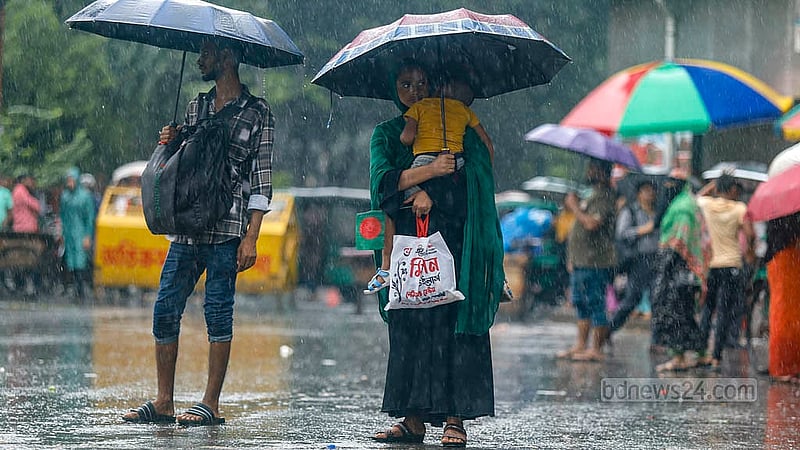 জুলাই আন্দোলনে আহতদের অবরোধ আর ঝুম বৃষ্টির মধ্যে ঢাকার শাহবাগে ছাতা হাতে শিশু কোলে নিয়ে এক নারী। ছবি: মাহমুদ জামান অভি