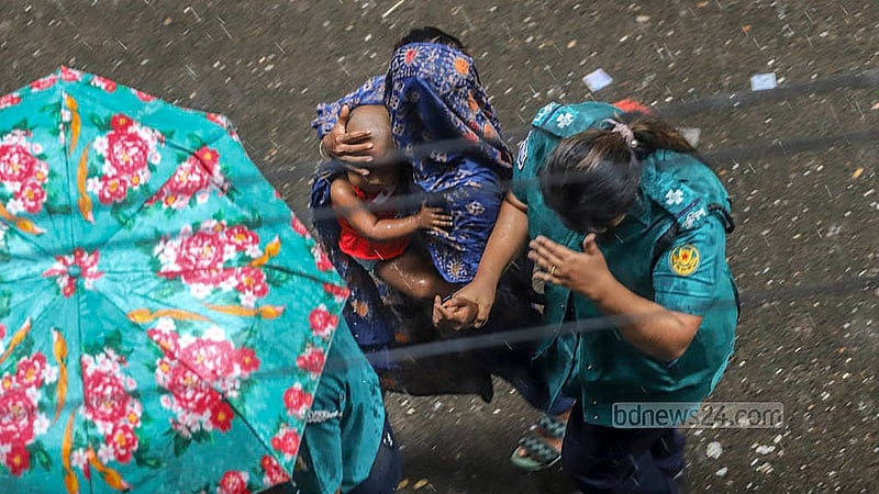 বৃষ্টির মধ্যেই আদালতে নেওয়া হচ্ছে এক নারী আসামিকে, কোলে তার শিশু সন্তান। বুধবার ঢাকার মুখ্য মহানগর হাকিম আদালত থেকে তোলা