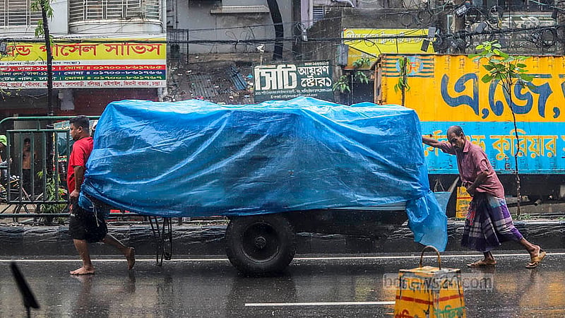 পুরান ঢাকার নর্থ সাউথ রোডে বুধবার বৃষ্টির মধ্যে ঠেলাগাড়ি নিয়ে যাওয়ার সময় মালামাল পলিথিনে ঢেকে দেন চালকেরা