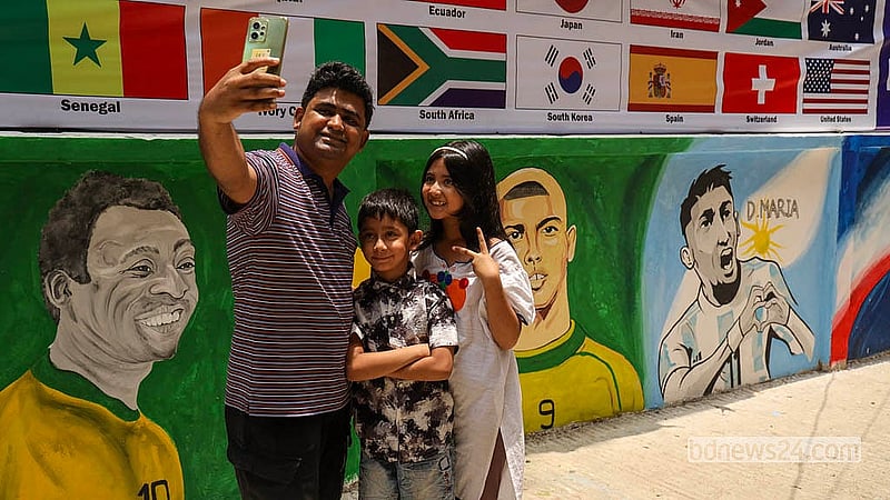 ঢাকার টিকাটুলীর ‘ফিফা গলি’তে পেলে, রোনালদো ও দি মারিয়ার ছবির সামনে দাঁড়িয়ে এক পরিবারের সেলফি তোলার আনন্দঘন মুহূর্ত।