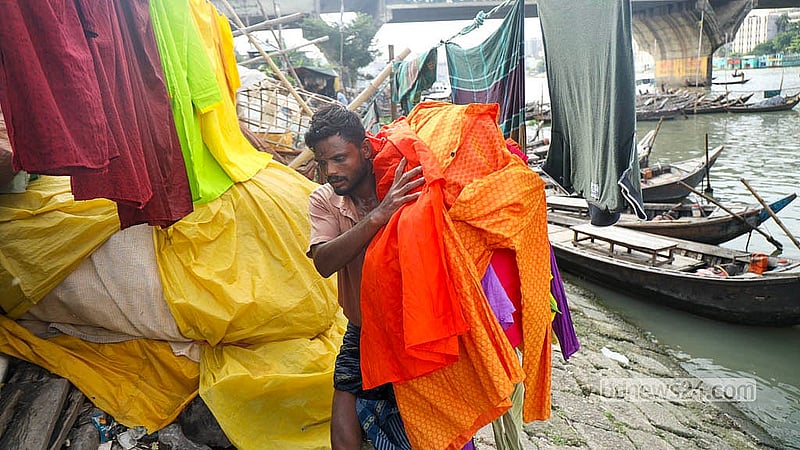 বুড়িগঙ্গা নদীতে ধোয়া কাপড় শুকানোর পর স্তূপ করে নিয়ে যাচ্ছেন ধোপাদের একজন