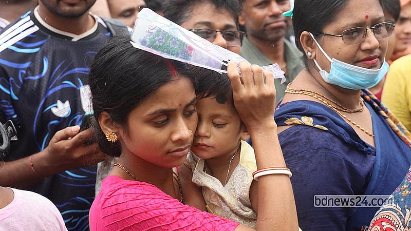 যমুনা ফিউচার পার্কের ভিসা কেন্দ্রের বাইরে ফাইল ফোল্ডার মাথায় দিয়ে সন্তানকে কোলে নিয়ে লাইনে দাঁড়িয়ে আছেন এক মা