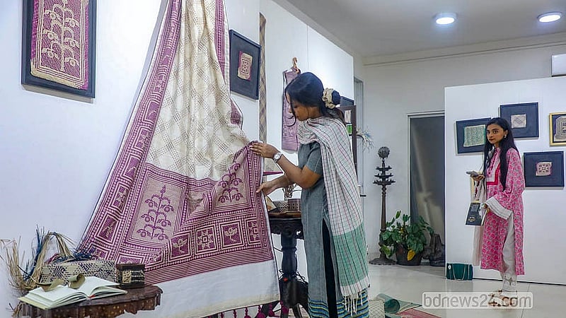 শীতলপাটির নকশায় তৈরি শাড়ি দেখছেন একজন। প্রদর্শনীর পাশাপাশি বেচা হচ্ছে এসব পণ্য
