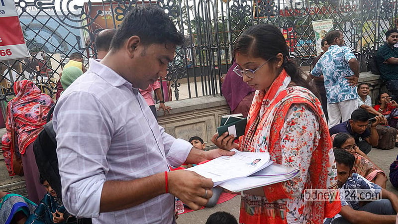 যমুনা ফিউচার পার্কের ভিসা কেন্দ্রের বাইরে ফুটপাতে দাঁড়িয়ে থাকা নিজেদের ফরমের তথ্য মিলিয়ে দেখছেন আবেদনকারীরা