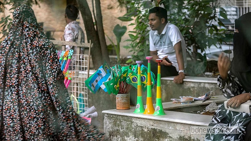 ঢাকার লালবাগ এলাকায় ব্রাজিল ও আর্জেন্টিার পতাকা এবং বাঁশি নিয়ে বসেছেন এক বিক্রেতা