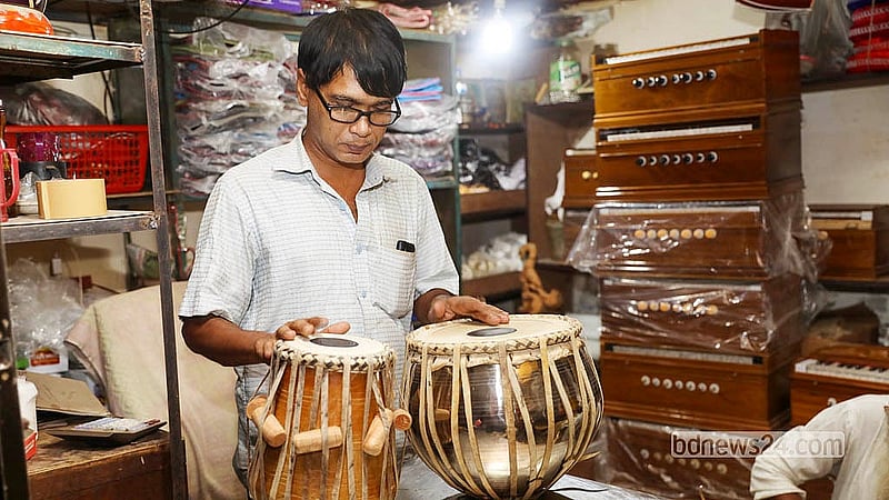 পুরান ঢাকার শাঁখারীবাজারের দোকানে সাজিয়ে রাখা বড় বড় ঢাক ও ঢোলের মাঝে বসে তবলার টিউনিং ও চামড়া পরখ করছেন কারিগর