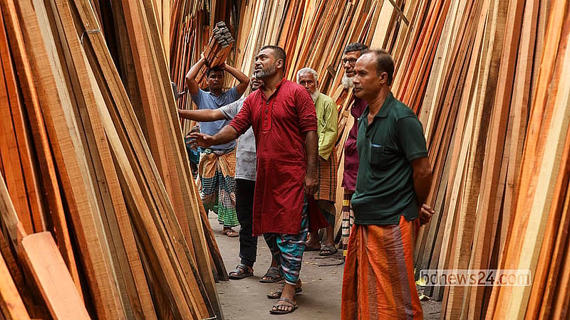 মুন্সীগঞ্জের দিঘীরপাড় হাটে বিক্রির জন্য থরে থরে সাজিয়ে রাখা চেরা কাঠের স্তূপের মাঝে দাঁড়িয়ে কাঠের মান ও মাপ পরীক্ষায় ক্রেতারা