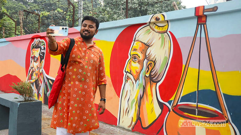 ঢাকার সেগুনবাগিচায় ফুটপাত সংলগ্ন দেয়ালে আঁকা ফকির লালন ও সত্যজিৎ রায়ের প্রতিকৃতির সঙ্গে ছবি তুলছেন পথচারীরা। ছবি: শামছুল হক রিপন