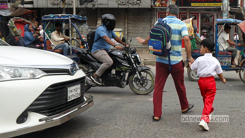 রাজধানীর মালিবাগে হাতের ইশারায় গাড়ি থামিয়ে সন্তানকে নিয়ে রাস্তা পার হচ্ছেন এক অভিভাবক। ছবি: শামছুল হক রিপন