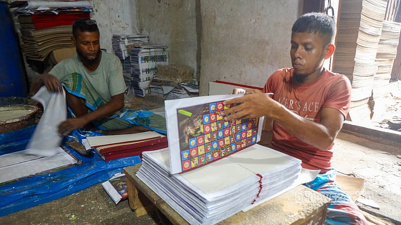 পুরান ঢাকার চকবাজারের ছোট কাটরায় লুডু বোর্ড তৈরি করছেন কারিগররা। ছাপানো কাগজ কয়েকটি ধাপে মোটা হার্ডবোর্ডে লাগিয়ে তৈরি করা হয় এসব বোর্ড। ছবি: শামছুল হক রিপন