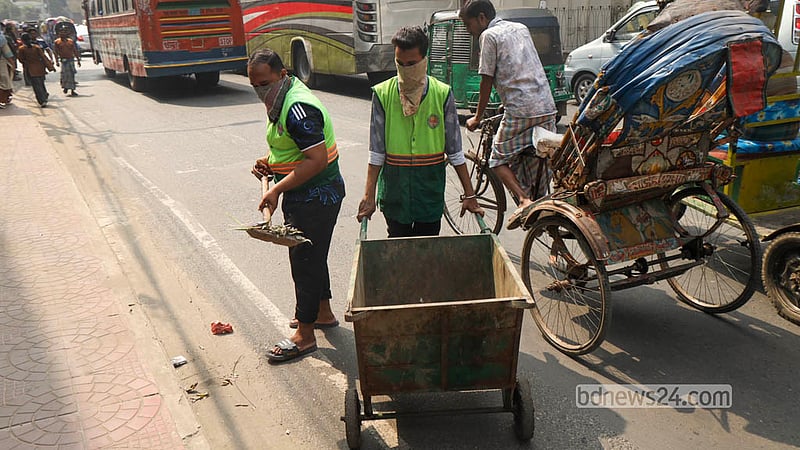 রাজধানীর টিকাটুলী এলাকায় প্রধান সড়কের পাশের জমে থাকা আবর্জনা পরিষ্কার করছেন ঢাকা দক্ষিণ সিটি করপোরেশনের কর্মীরা। ছবি: শামছুল হক রিপন