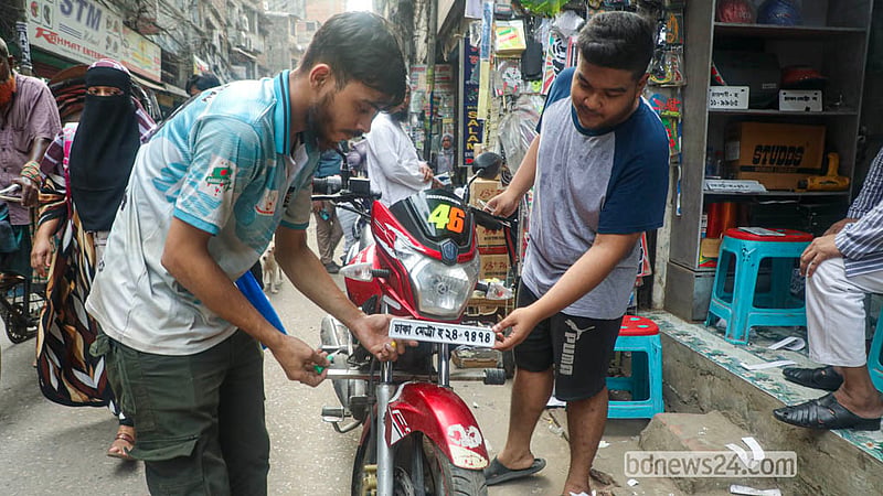 মোটরসাইকেলের সামনে নম্বর প্লেট সাঁটিয়ে দিচ্ছেন এক দোকানি। বংশাল এলাকায় প্রতিদিন বিক্রি হচ্ছে কয়েক হাজার নম্বর প্লেট।&amp;nbsp;&amp;nbsp; ছবি: আব্দুল্লাহ আল মমীন