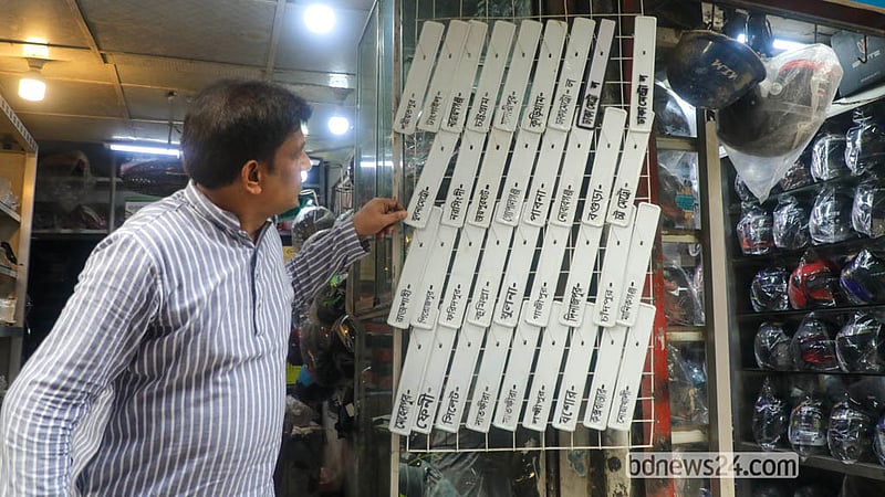 বংশাল এলাকার এক দোকানে মোটরসাইকেলের সামনের অংশের জন্য নম্বর প্লেট দেখছেন এক চালক। সেখানে জেলাভিত্তিক নম্বর প্লেট সাজানো রয়েছে।&amp;nbsp;&amp;nbsp; ছবি: আব্দুল্লাহ আল মমীন