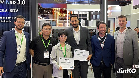 Six people at a Jinko ESS exhibition booth, two holding MoU certificates with UCB logos.
