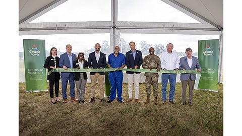 Nine officials hold a ribbon under a marquee at the Robins Battery Facility ceremony.
