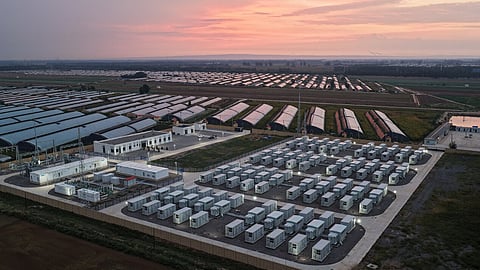 Rows of white battery containers and a substation at a storage site at dusk.