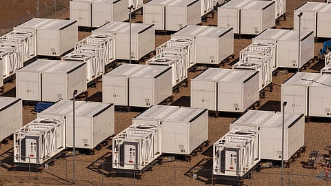 Rows of white battery containers with cooling units on a gravel pad.