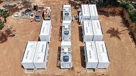 Aerial view of white battery containers standing in rows on a cleared earth site.