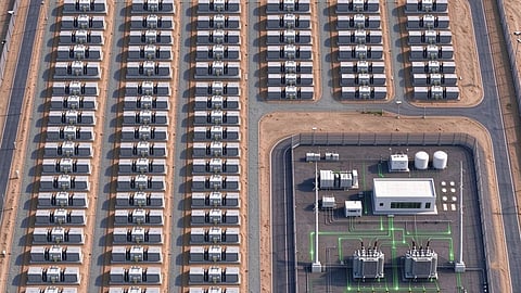 Aerial rendering of battery units in long rows beside a fenced substation in the desert.