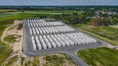 Aerial view of rows of white battery containers beside fields and village houses.