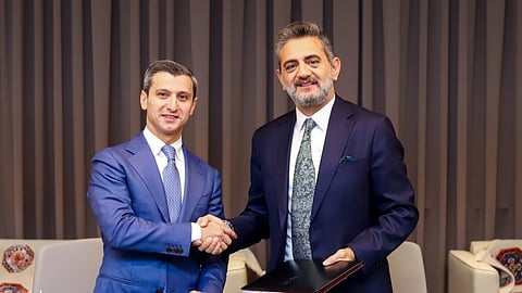 Two executives in blue suits shake hands in front of a grey curtain.