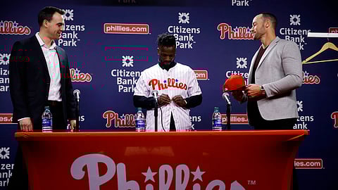 Philadelphia Phillies new outfielder Andrew McCutchen, center, accompanied by general manager Matt Klentak, left, and manager Gabe Kapler, puts on his uniform during a news conference in Philadelphia, Tuesday, Dec. 18, 2018. McCutchen and the Philadelphia Phillies finalized a back-loaded $50 million, three-year contract, a deal that includes a team option for 2022. (AP Photo/Matt Rourke)