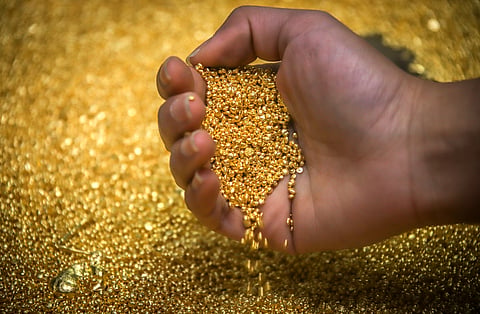 A worker checks gold granules at a refinery smelter.