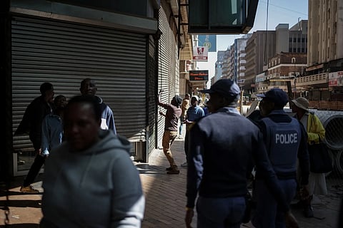 South African police watch a worker shutter a shop during a demonstration against undocumented migrants in Johannesburg