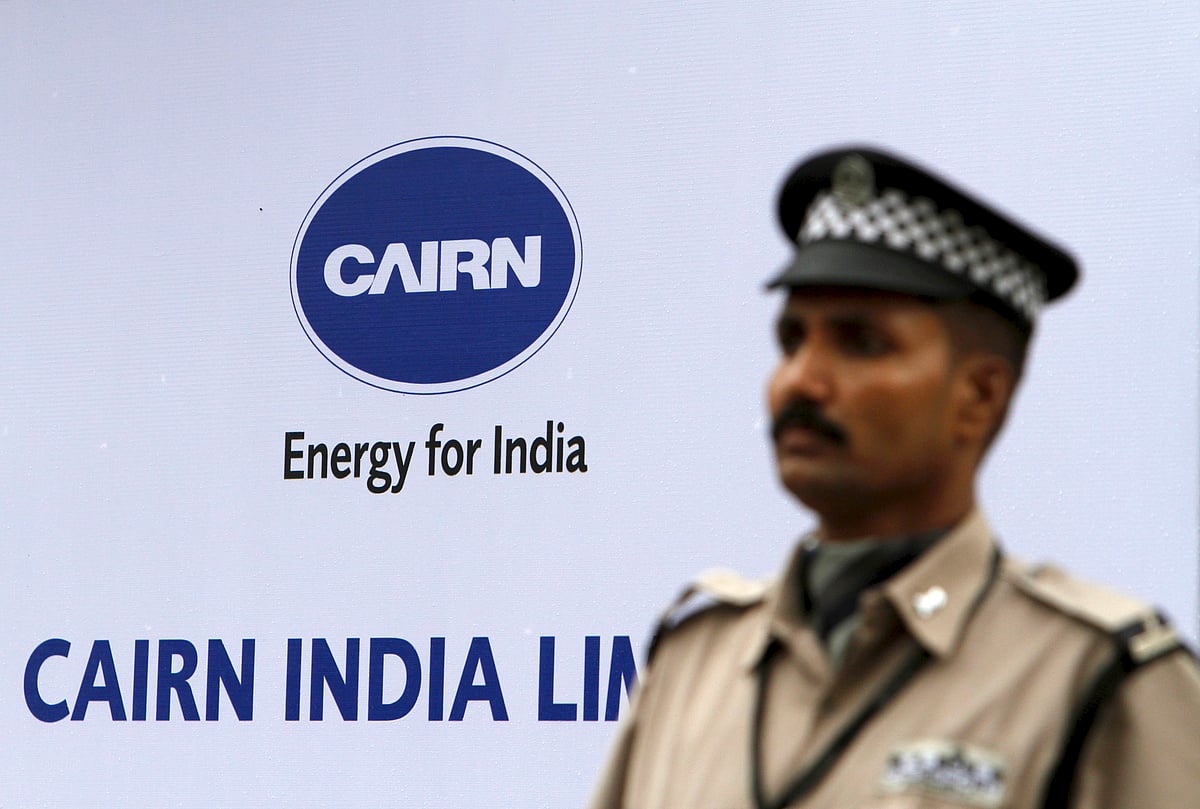 A security guard stands in front of a sign featuring the Cairn India Ltd. (Photographer: Adeel Halim/Bloomberg)