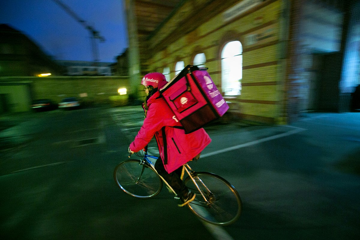 An employee rides a bicycle while carrying a backpack food delivery box outside the headquarters of Foodora, the food courier service operated by Delivery Hero Holding GmbH, in Berlin, Germany. (Photographer: Krisztian Bocsi/Bloomberg)