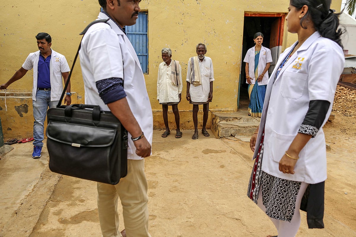 Villagers and medical staff stand outside a building in Pancharala, on the outskirts of Bengaluru, India, on June 9, 2017. (Photographer: Dhiraj Singh/Bloomberg)