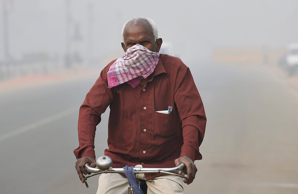 A man covers his nose with a handkerchief to protect himself from heavy smog and air pollution while cycling on the road near India Gate. (Image: PTI)