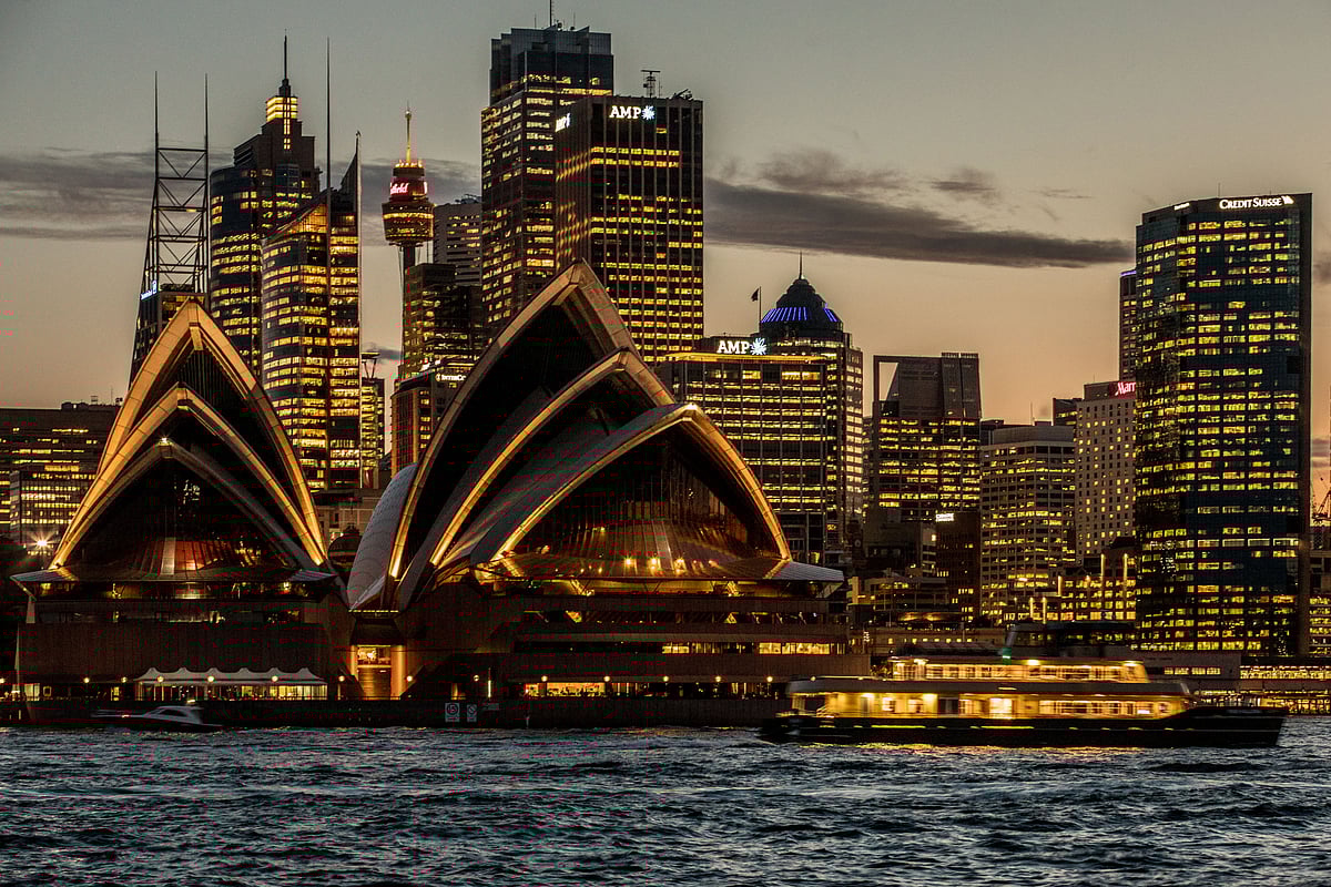 The Sydney Opera House, foreground, and buildings in the financial district stand illuminated at dusk in Sydney, Australia. (Photographer: Cole Bennetts/Bloomberg)