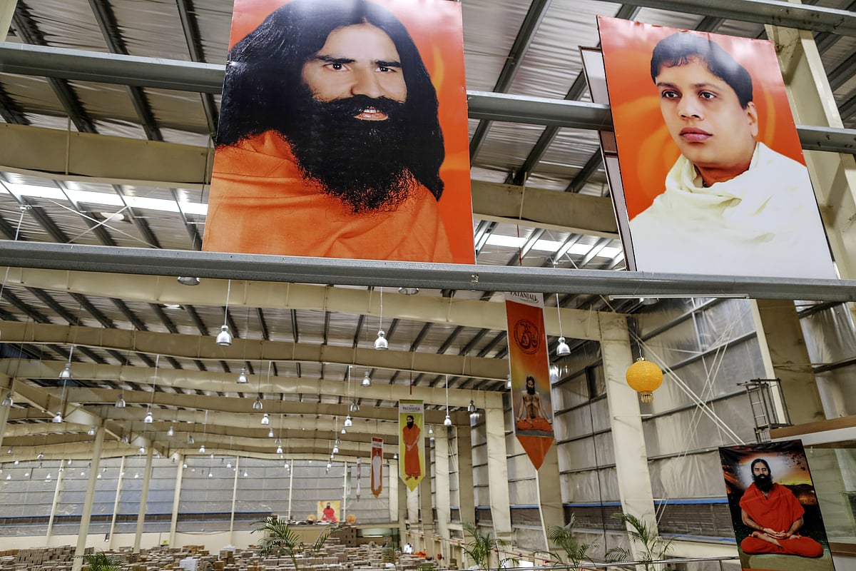 Posters depicting yoga guru Baba Ramdev, top left, and Acharya Balkrishna Ji, chief executive officer of Patanjali Ayurved Ltd., top right, are displayed inside a warehouse operated by the company. (Photographer: Dhiraj Singh/Bloomberg) &nbsp;
