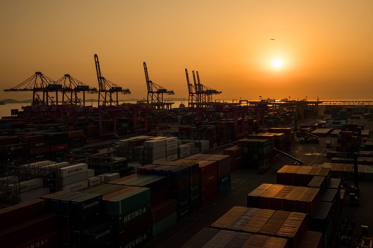 Containers sit stacked beneath gantry cranes. (Photographer: SeongJoon Cho/Bloomberg) &nbsp;
