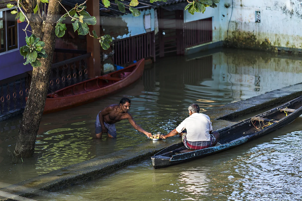 A man standing in floodwater shares a tray of tea with another man sitting in a canoe in Kainakary village in the district of Alappuzha, Kerala. (Photographer: Prashanth Vishwanathan/Bloomberg)