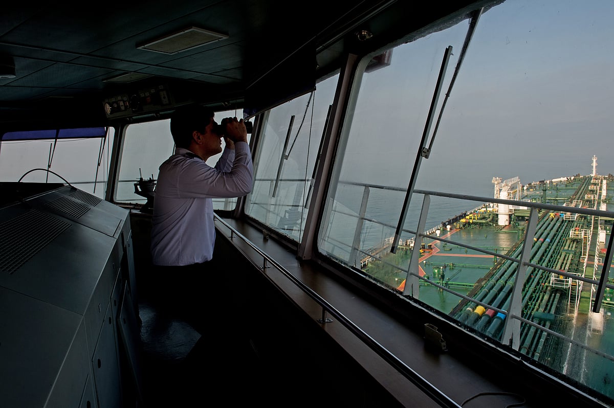 A crew member uses binoculars on the bridge of an  oil tanker. (Photographer: Ali Mohammadi/Bloomberg)