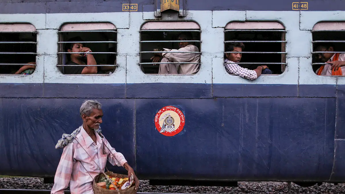 A food vendor walks past passengers sitting at the windows of the Kalka Mail train as it stands at Allahabad Junction station in Allahabad, Uttar Pradesh, India. (Photographer: Dhiraj Singh/Bloomberg)