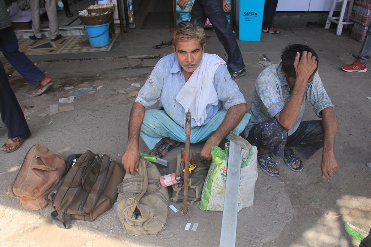 An electrician waits with his assistant and tools by the roadside looking for work near  the Labour Chowk at Sector-49, Noida. (Photographer: Nishant Sharma/BloombergQuint)
