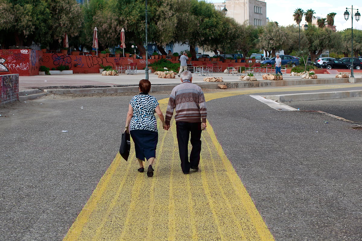 An elderly couple walk along a waterfront. (Photographer: Kostas Tsironis/Bloomberg)&nbsp;