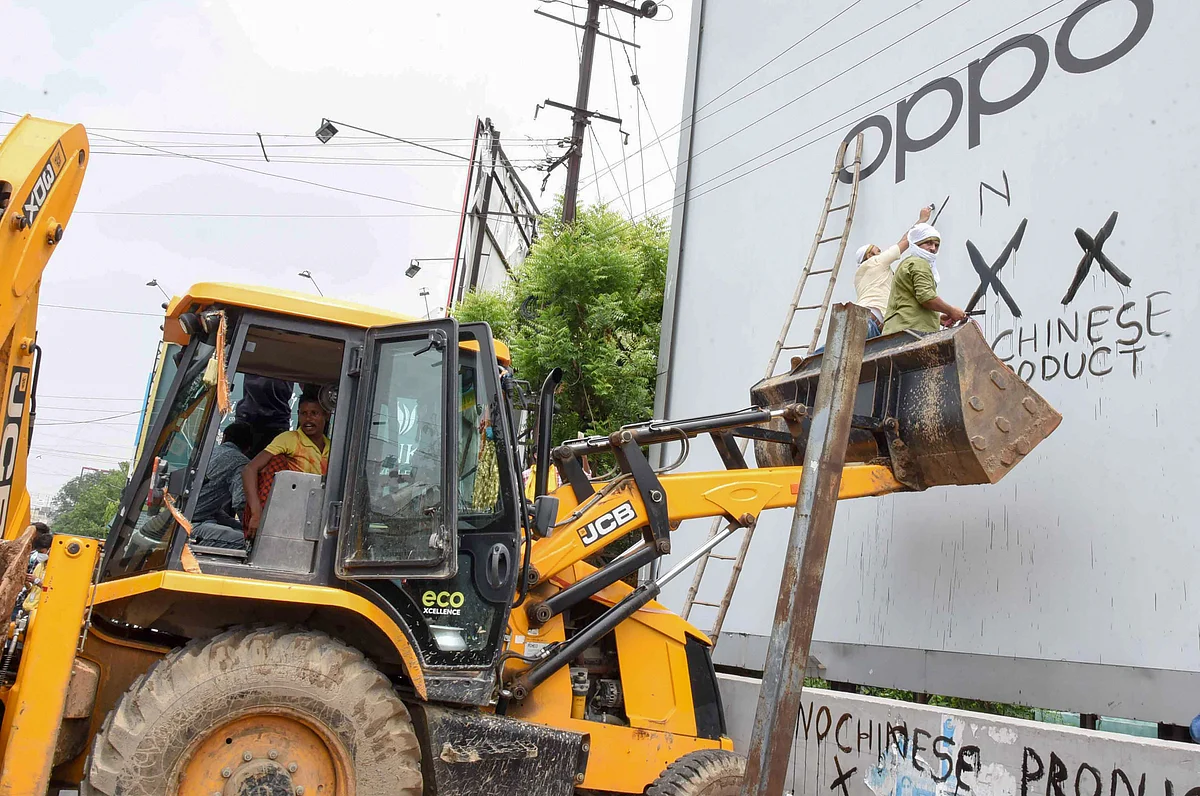 A political activist climbs a JCB machine to blacken a banner of a Chinese mobile phone manufacturer, in Patna, on June 18, 2020. (Photograph: PTI)