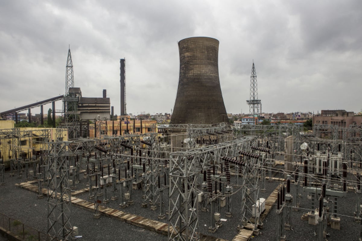 The cooling tower of a power plant stands behind an electrical grid in Patna. (Photographer: Prashanth Vishwanathan/Bloomberg)