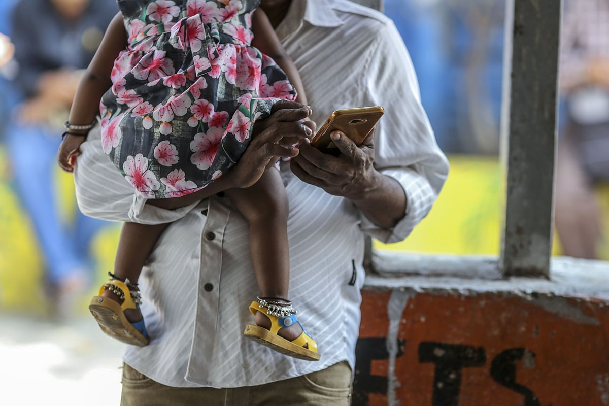 A man uses a smartphone while carrying a child in Mumbai, on Feb. 15, 2020. (Photographer: Dhiraj Singh/Bloomberg)