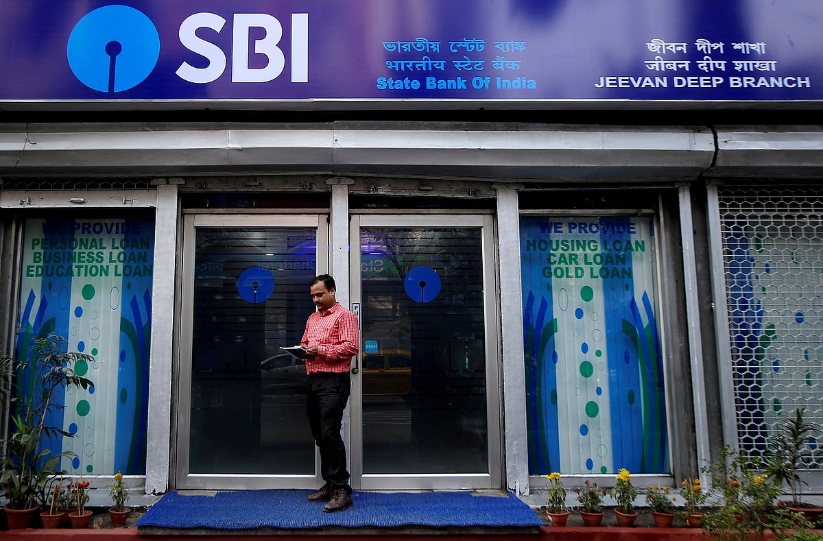 <div class="paragraphs"><p>A man checks his mobile phone in front of a State Bank of India branch in Kolkata, India. (Source: Reuters)</p></div>